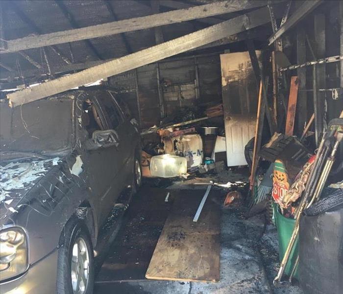 Smoke and soot damages inside a garage, where the ceiling has collapsed onto a car