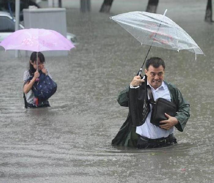 A couple walking through waist-high water holding umbrellas