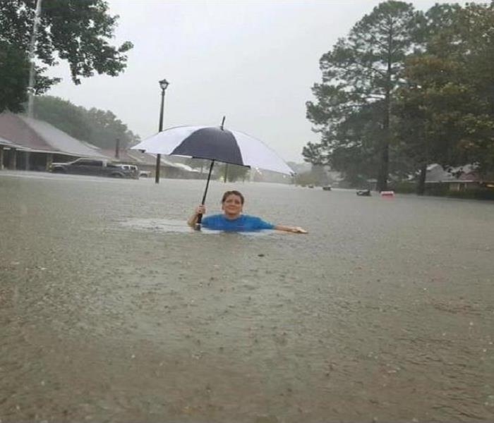 A woman, chest deep in floodwaters, carrying an umbrella