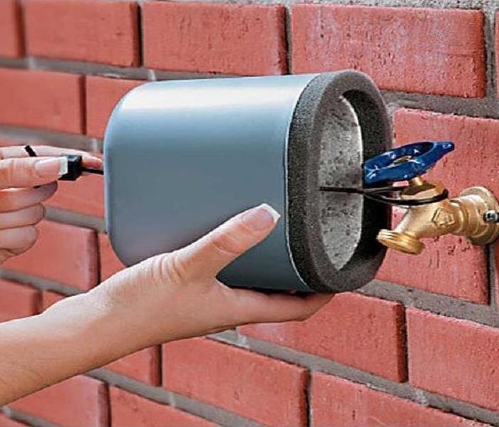 Homeowner putting a cover over an outdoor spigot.